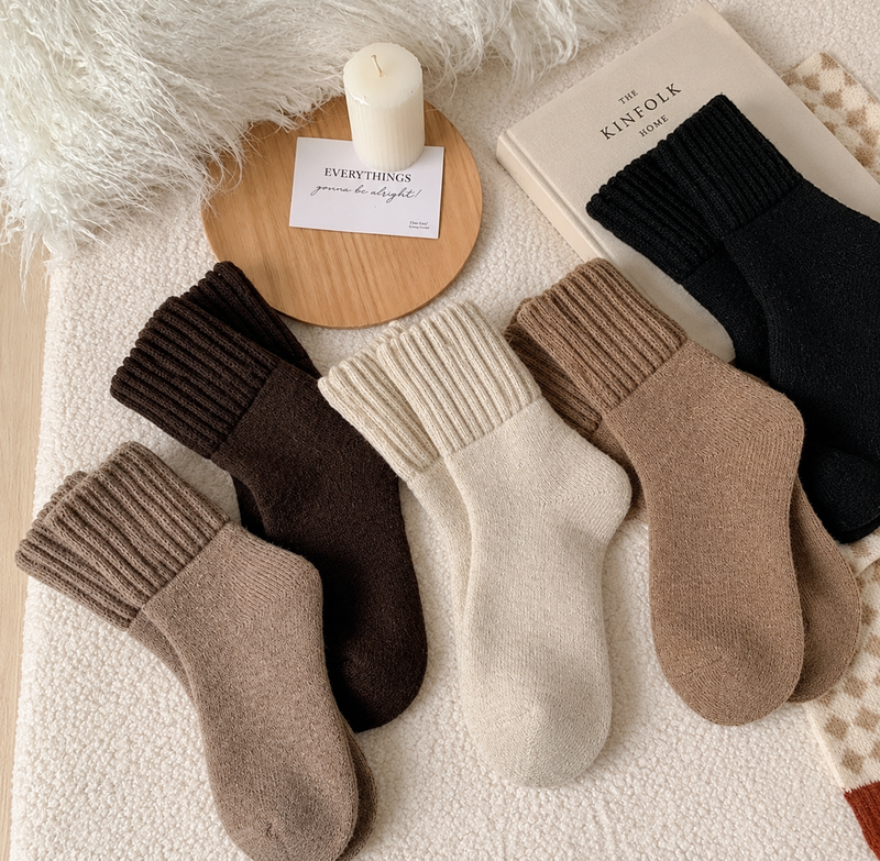 The 5-pair mixed set: cozy fold-over cuff socks in taupe, brown, cream, beige and black, laid on a soft blanket next to a candle and a book