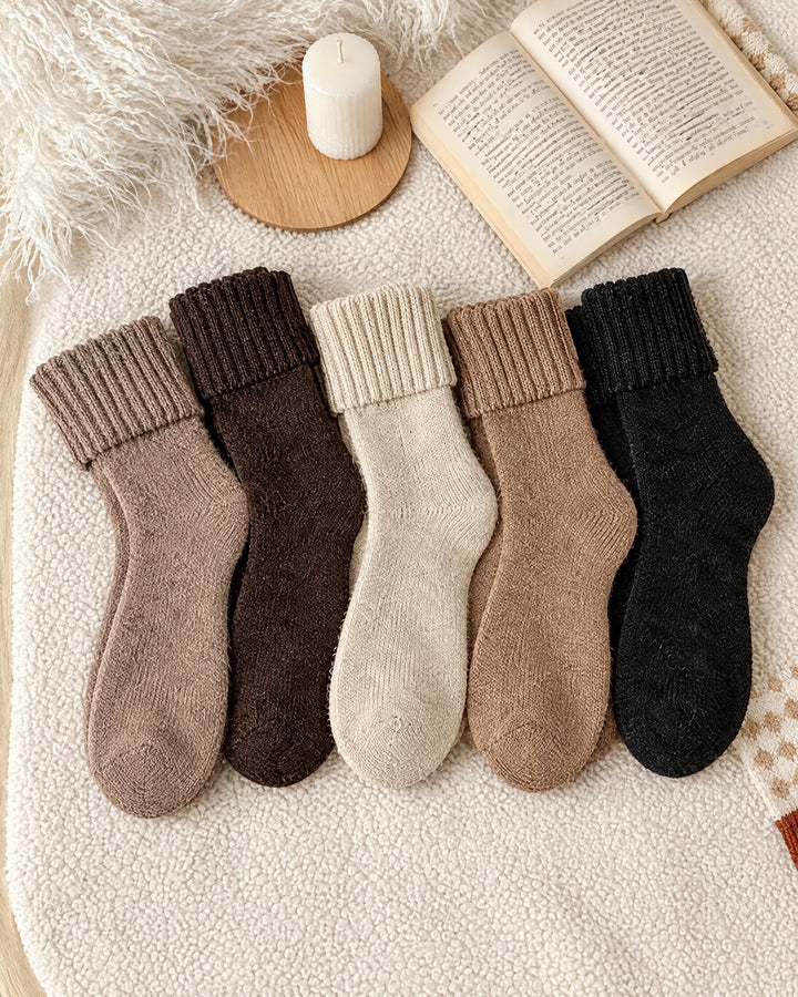 Five pairs of thick fold-over cuff socks in cream, beige, taupe, brown and black laid on a cream blanket